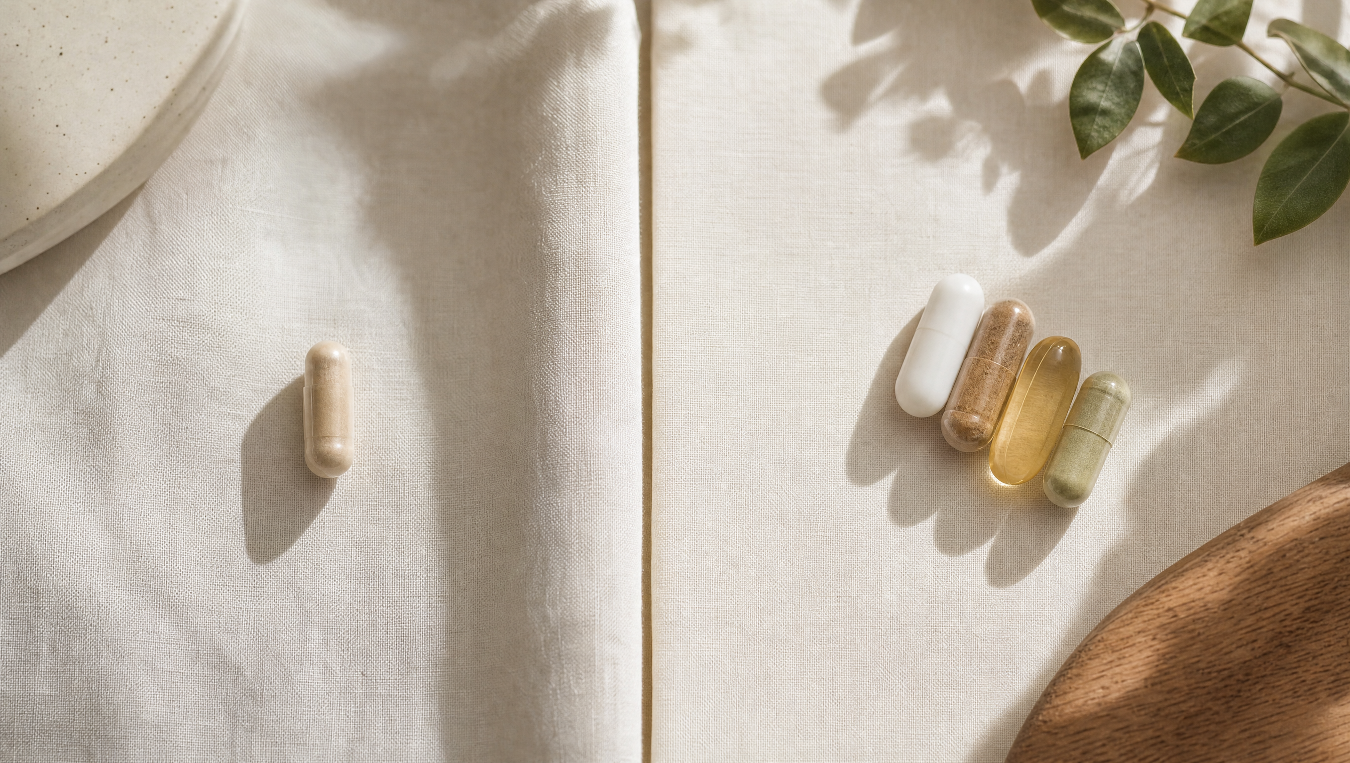 Een enkele capsule tegenover een kleine geordende cluster capsules op cremekleurig linnen — multivitamine versus gerichte supplement-stack