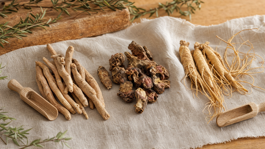 Drie gedroogde adaptogeen-wortels (ashwagandha, rhodiola, ginseng) op linnen en eikenhout — adaptogenen vergeleken
