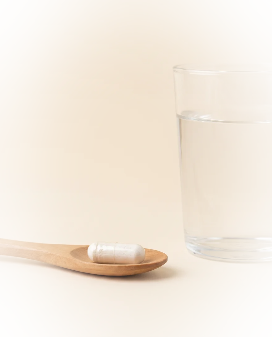 Capsule Magnesium Ultimate op een houten lepel naast een glas water