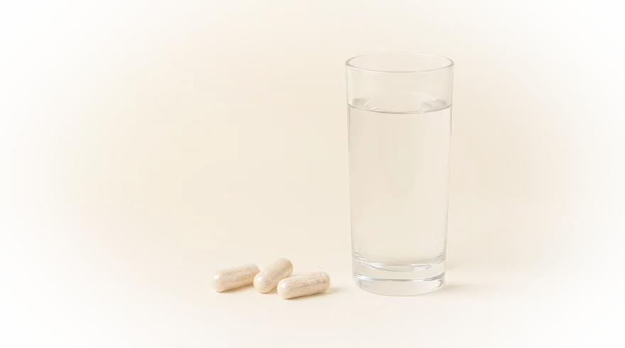 Drie psylliumvezel-capsules naast een groot glas water